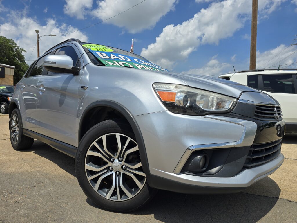 Silver SUV at a car lot with bright green sale stickers on the windshield reading 'BAD CAR' and '2017'.