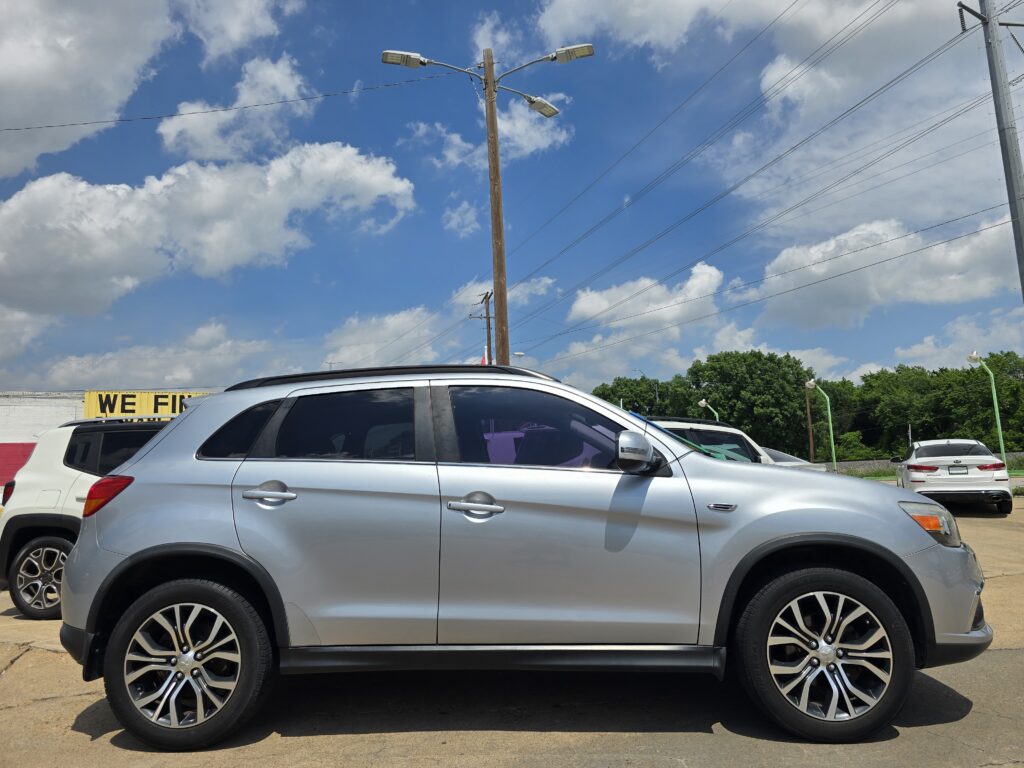 Silver SUV in a parking lot with a tall wooden utility pole and streetlights, blue sky and clouds above.