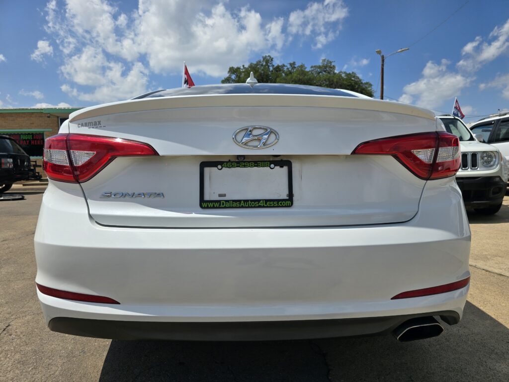 Rear view of a white Hyundai Sonata at a car dealership, with a Dallas Autos 4 Less license plate frame visible on the back.