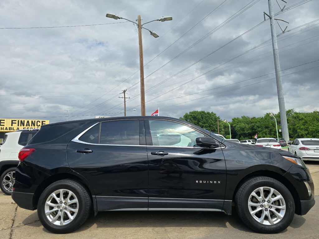 Side view of a black Chevrolet Equinox parked in a dealership lot beneath a cloudy sky with power lines above.
