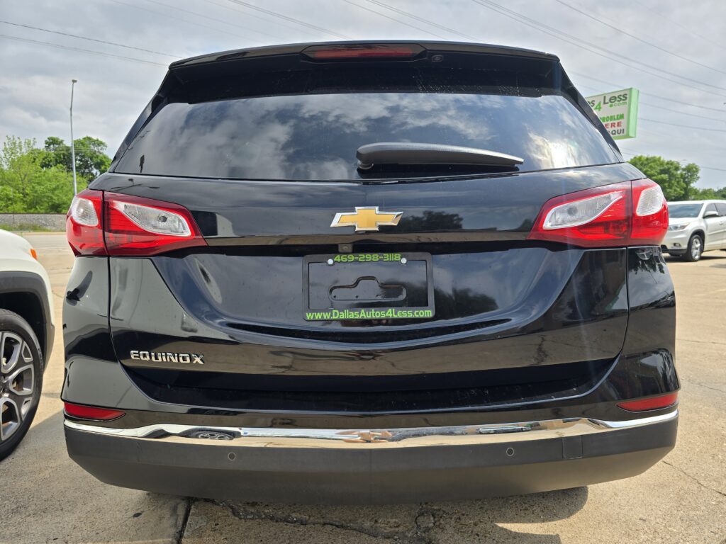 Rear view of a black Chevrolet Equinox with red tail lights, Chevrol​et emblem, and a dealership plate frame reading www.DallasAutos4Less.com in green text.
