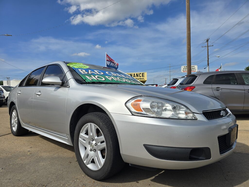 Silver sedan on a car dealership lot with a large 'BAD CREDIT NO PROBLEM' banner on its windshield against a bright blue sky and other vehicles in the background.