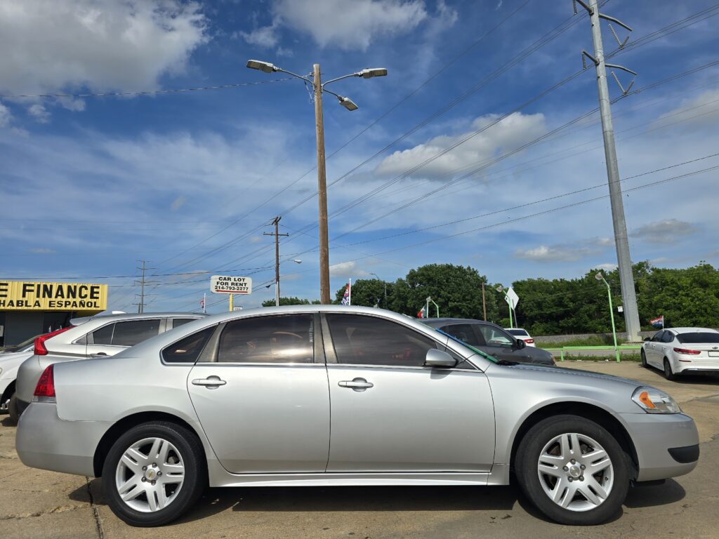 Row of parked silver sedans in a car lot under a blue sky with power lines and utility poles behind them.