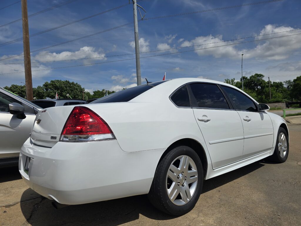 White sedan parked in a lot next to another car, under a blue sky with power lines overhead.