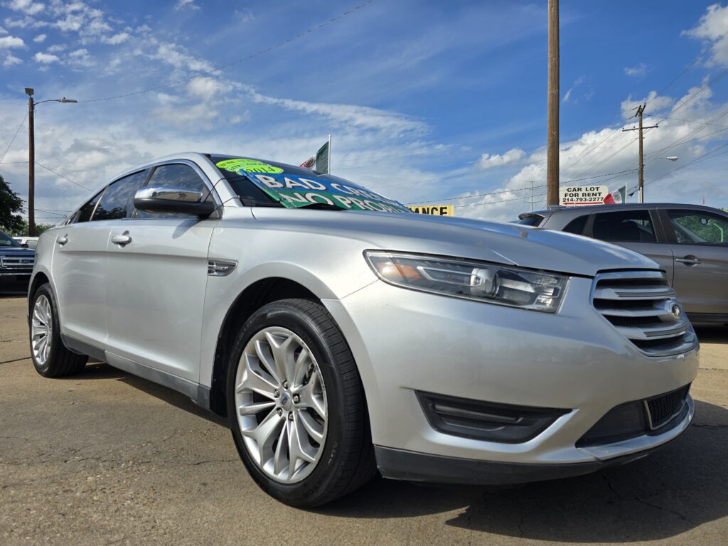 Silver sedan in a car lot with bright green sale signs visible on the windshield.