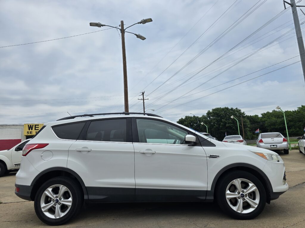 White SUV parked in a lot in the foreground, with a wooden utility pole and multiple power lines overhead against a cloudy sky.