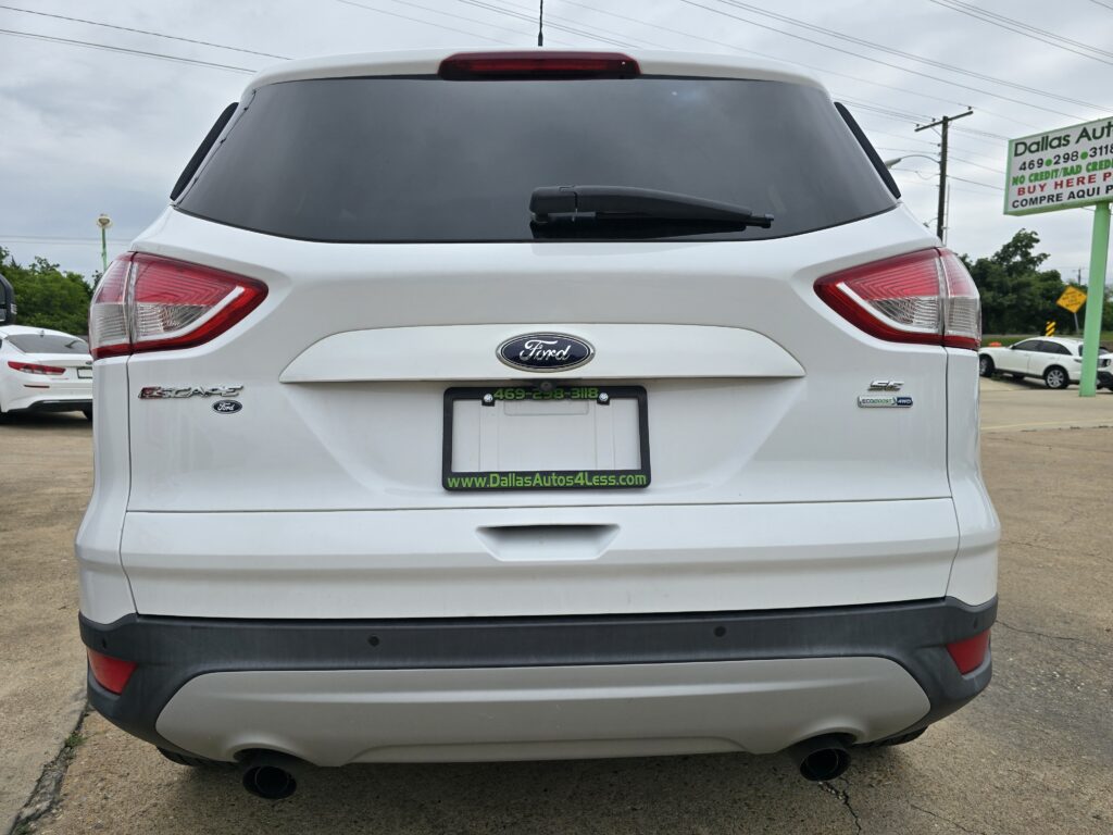 White Ford SUV rear view with tinted back window, red taillights, and green dealer plate frame reading www.DallasAutos4Less.com.