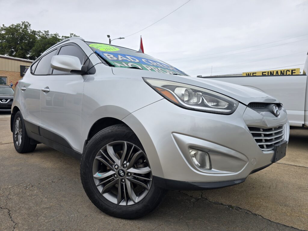 Silver Hyundai SUV parked on a dealership lot with bold sale signs on the windshield reading promotional text like 'BAD CREDIT' and 'NO PROBLEM'.