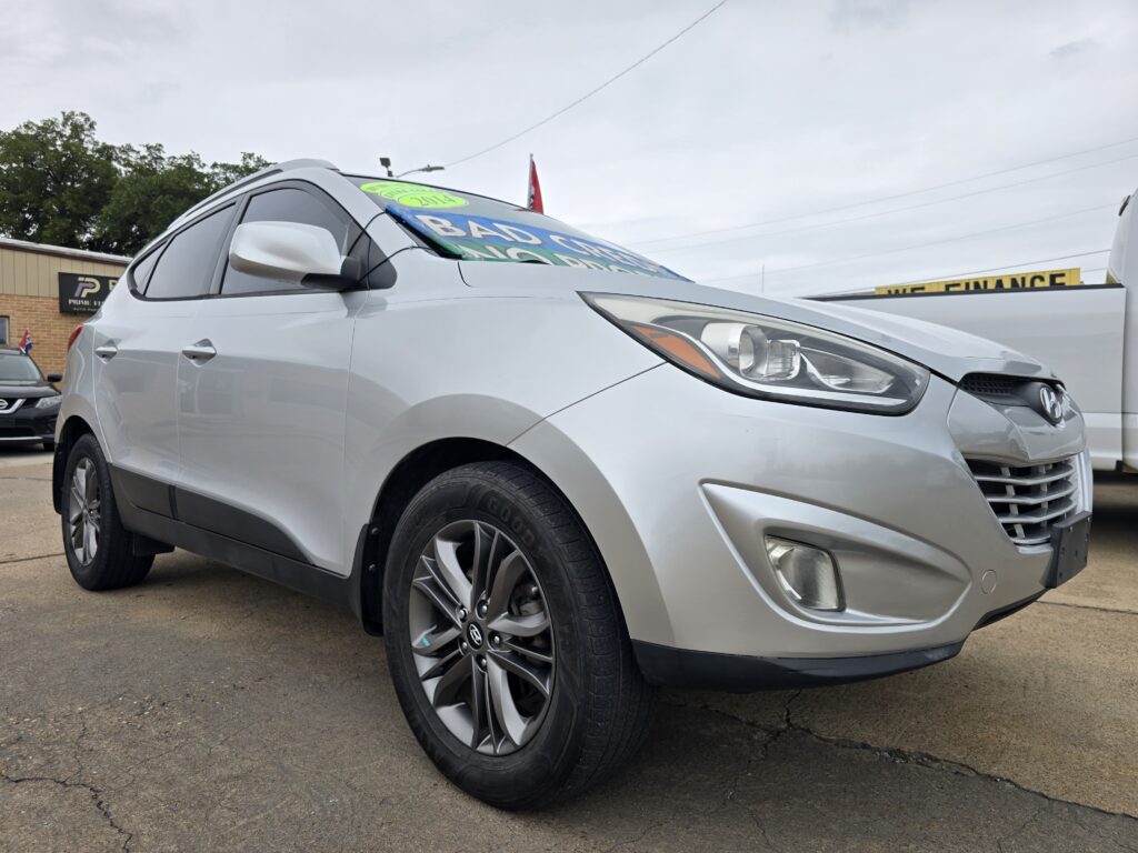 Close-up of a silver SUV on a dealership lot, front end visible with sale banners on the windshield and a 'We Finance' sign in the background.