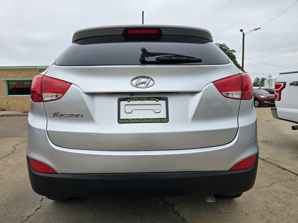 Rear view of a silver Hyundai Tucson with a dealer plate frame reading 'Dallas Autos 4 Less' in a parking lot.