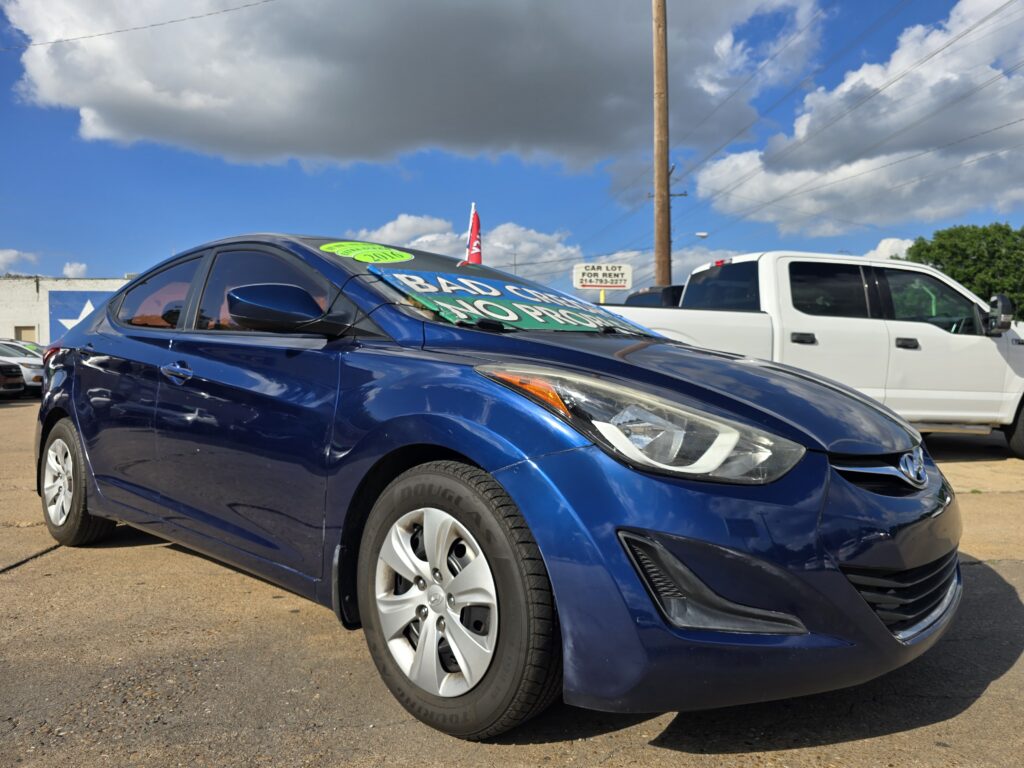 Blue car in the foreground at a used-car lot, with a bright green sale sign on the windshield.