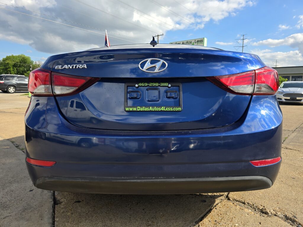 Blue Hyundai Elantra rear view in a car dealership lot, showing badge and green Dallas Autos 4 Less license plate frame.