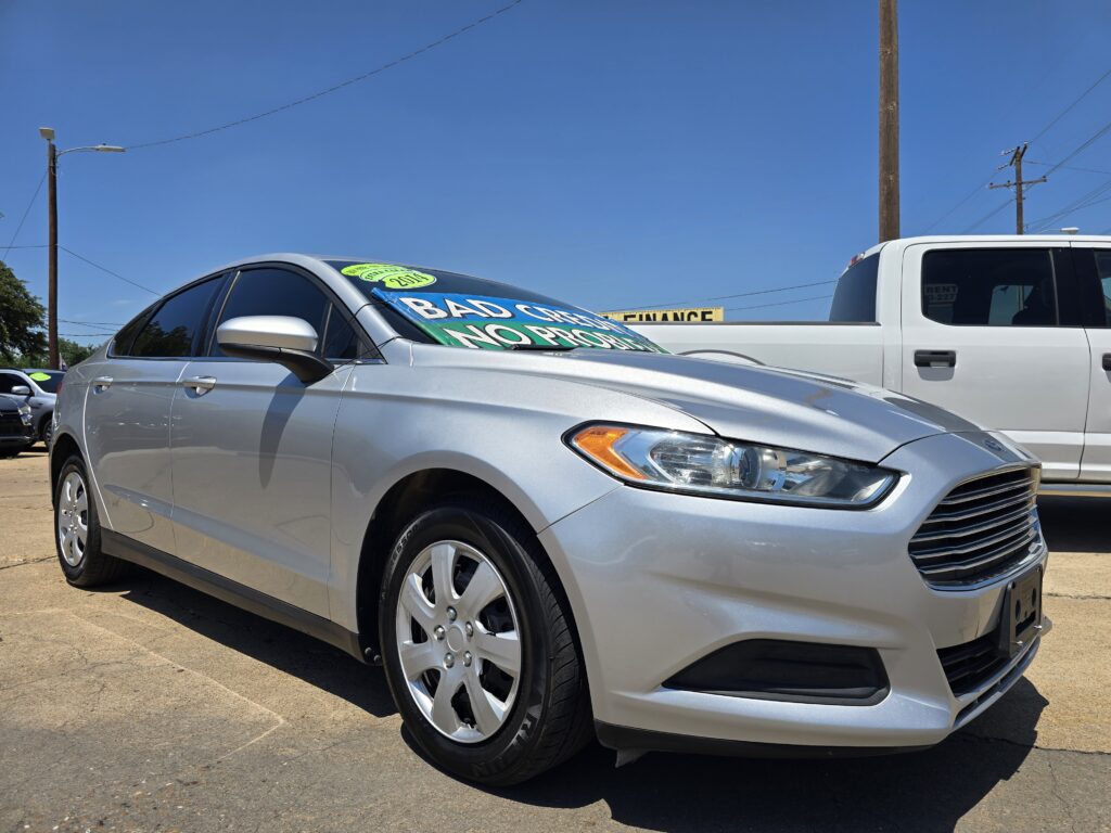 Silver sedan on a car lot with a bright green sale sign on the windshield against a clear blue sky. (Informative)