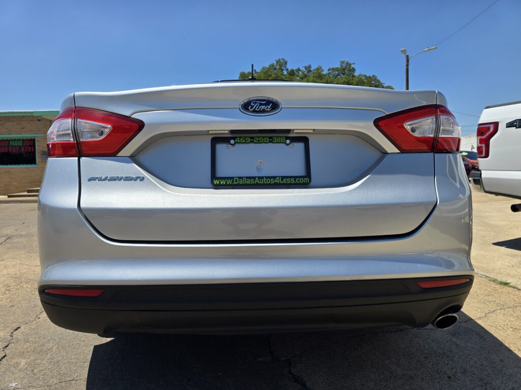 Rear view of a silver Ford Fusion with a green-framed license plate holder advertising DallasAutos4Less in a parking lot