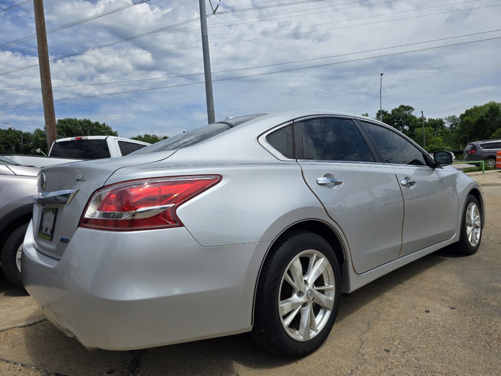 Rear-side view of a silver sedan in a parking lot, with a white vehicle behind and power lines overhead.