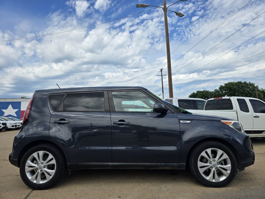 Dark gray SUV in a parking lot with other vehicles, under a cloudy blue sky and power lines in the background.