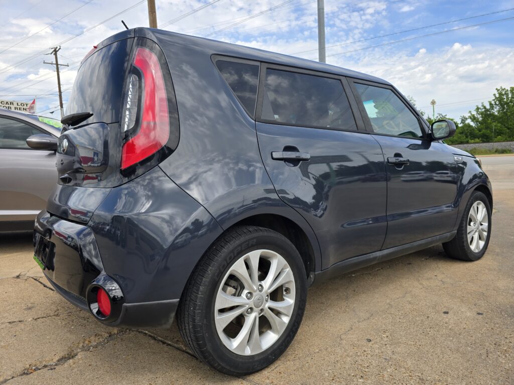 Rear-left side of a dark gray SUV showing the curved red tail light, rear bumper, large side window, and alloy wheel while parked on a paved lot.