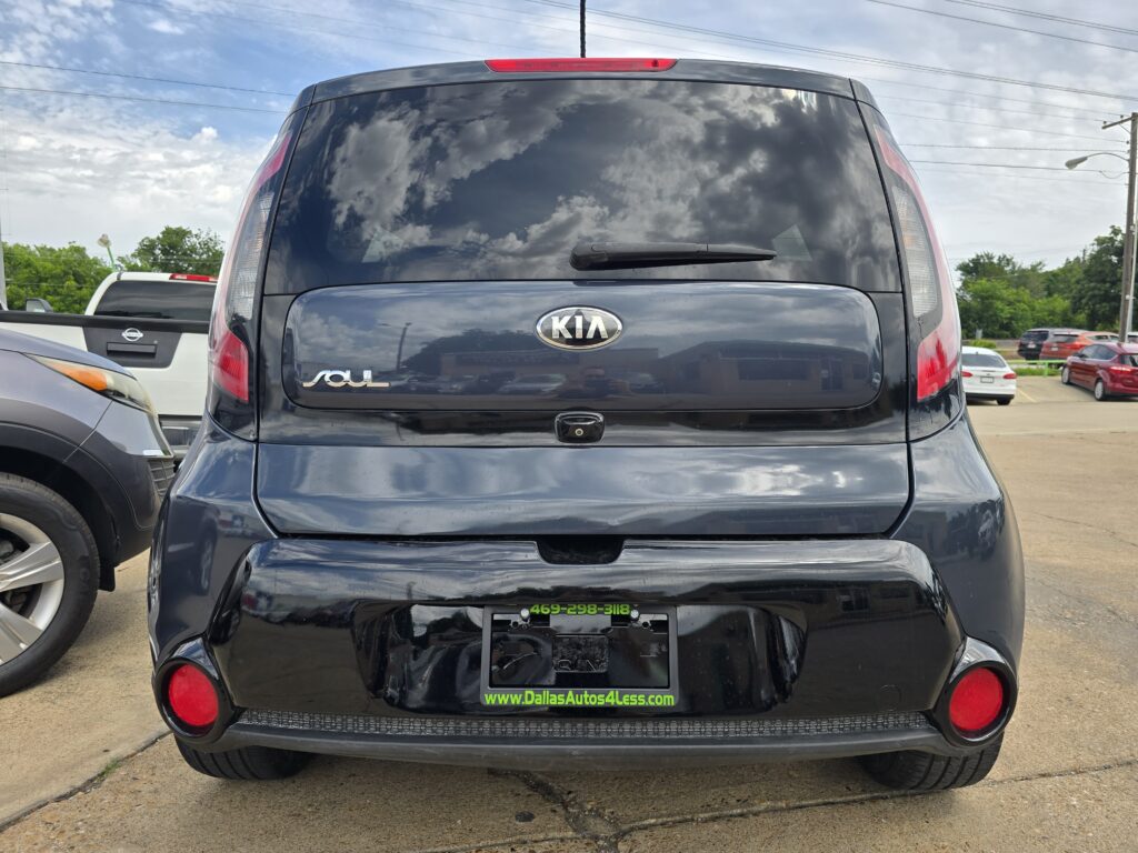 Rear view of a black Kia Soul SUV in a dealership parking lot, with Kia logo and dealership URL visible on the rear bumper area