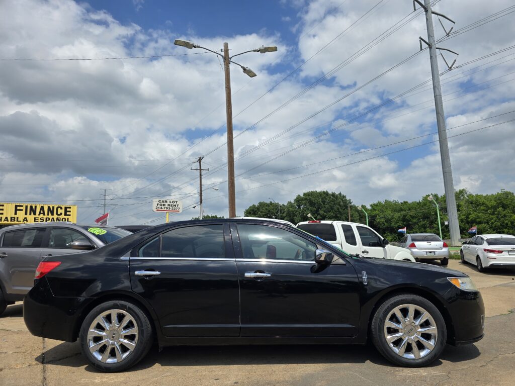 Black SUVs parked in a dealership lot with power poles and wires overhead, blue sky and clouds in the background.