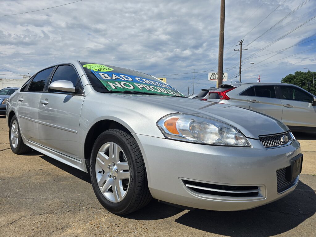 Silver sedan on a car dealership lot with a large windshield sign reading 'BAD CREDIT NO PROBLEM' and a cloudy sky above.