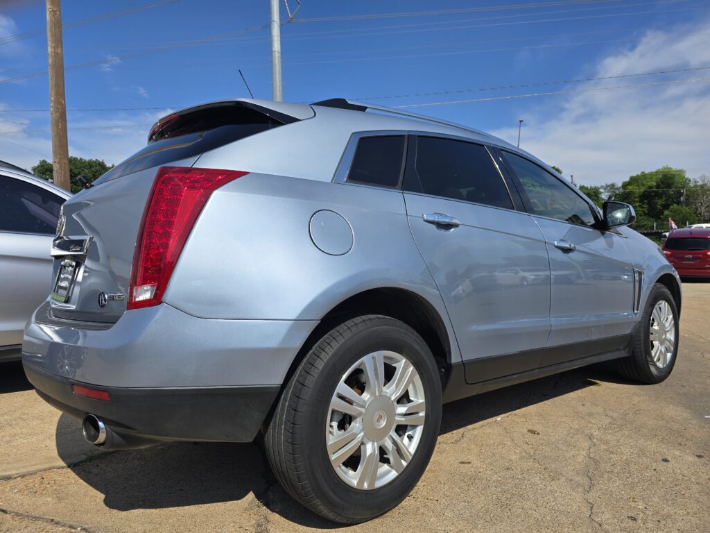 Rear-right quarter view of a silver Cadillac SUV parked on a sunny lot with power lines in the background