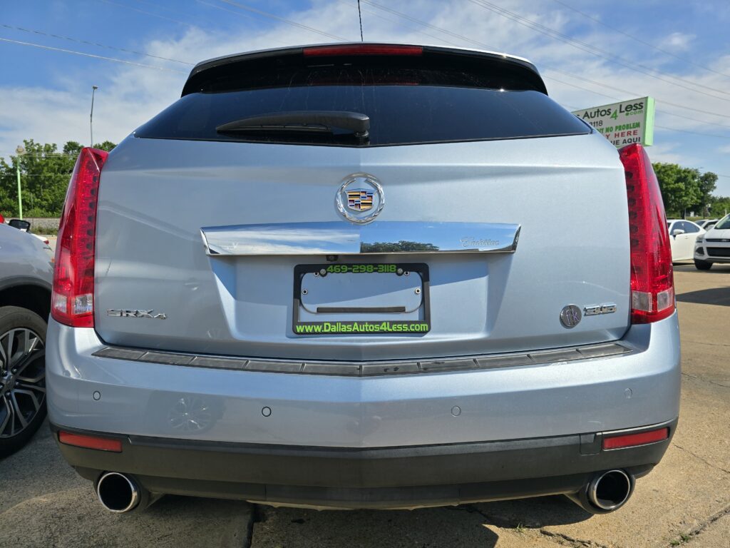 Rear view of a light blue Cadillac SUV showing the Cadillac emblem, chrome trim, and dual exhausts at the bottom corners