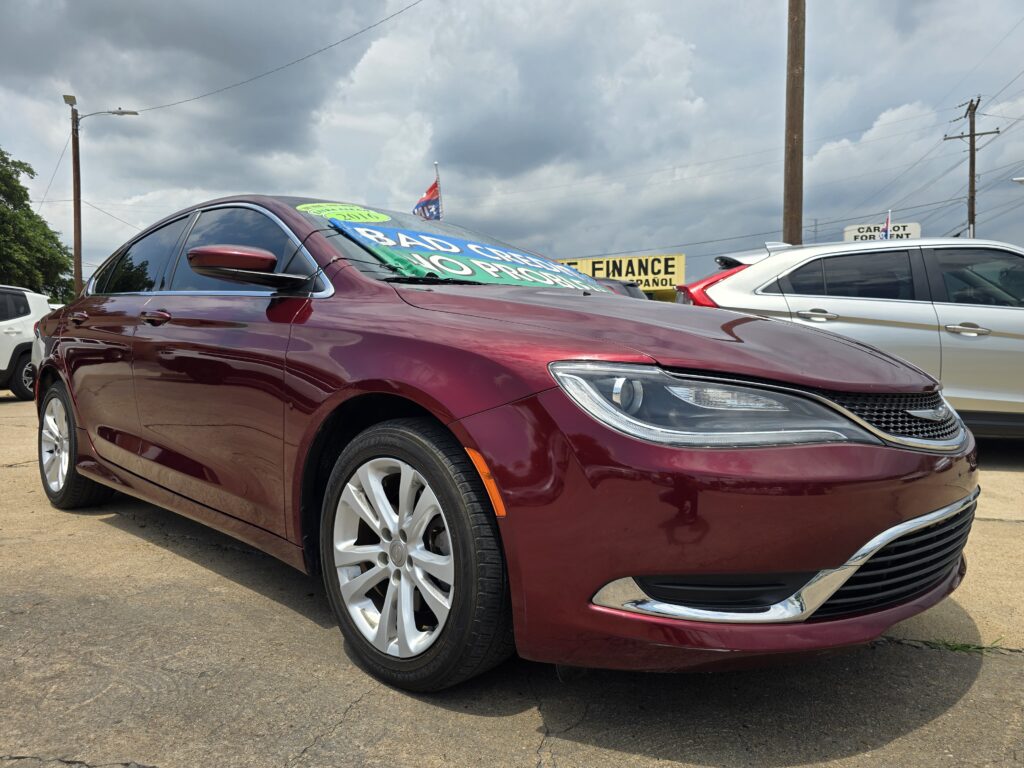 Maroon sedan at a dealership with large green sale banners on the windshield; overcast sky above.