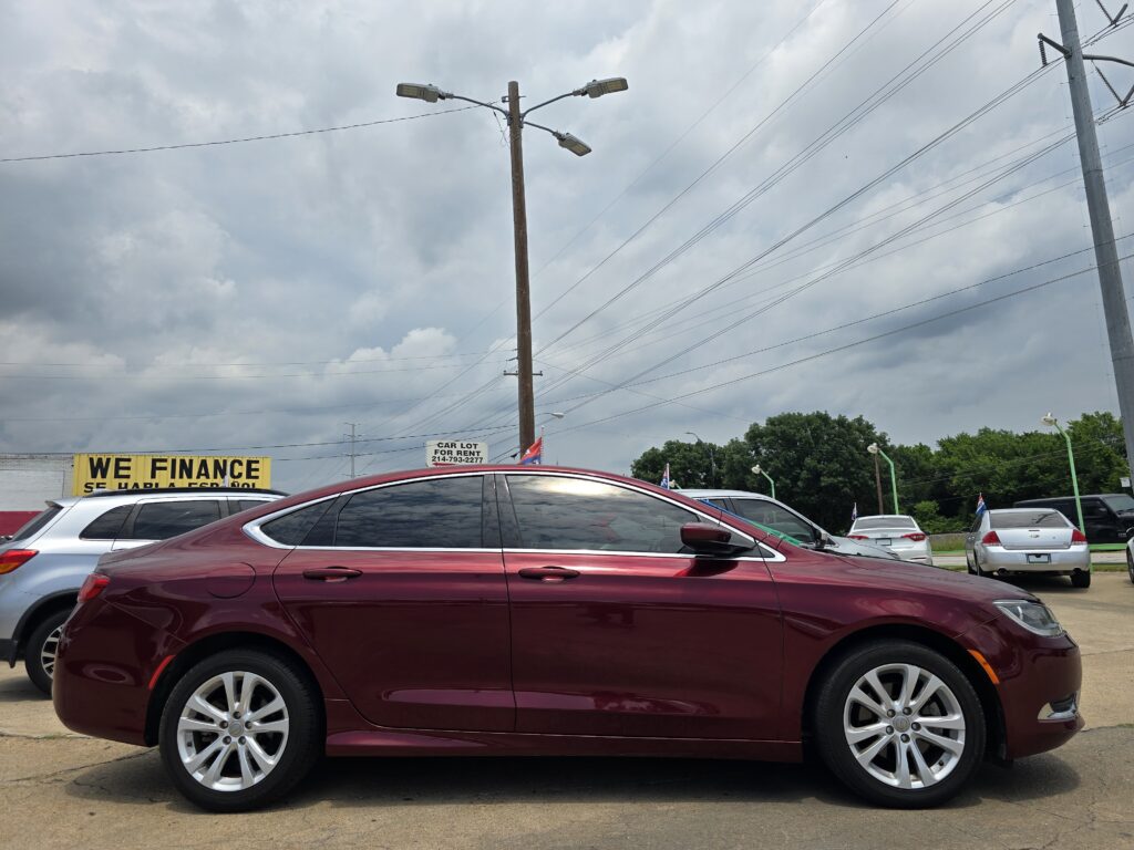 Red sedan in a dealership lot with a cloudy sky and utility poles; yellow 'WE FINANCE' sign in background.