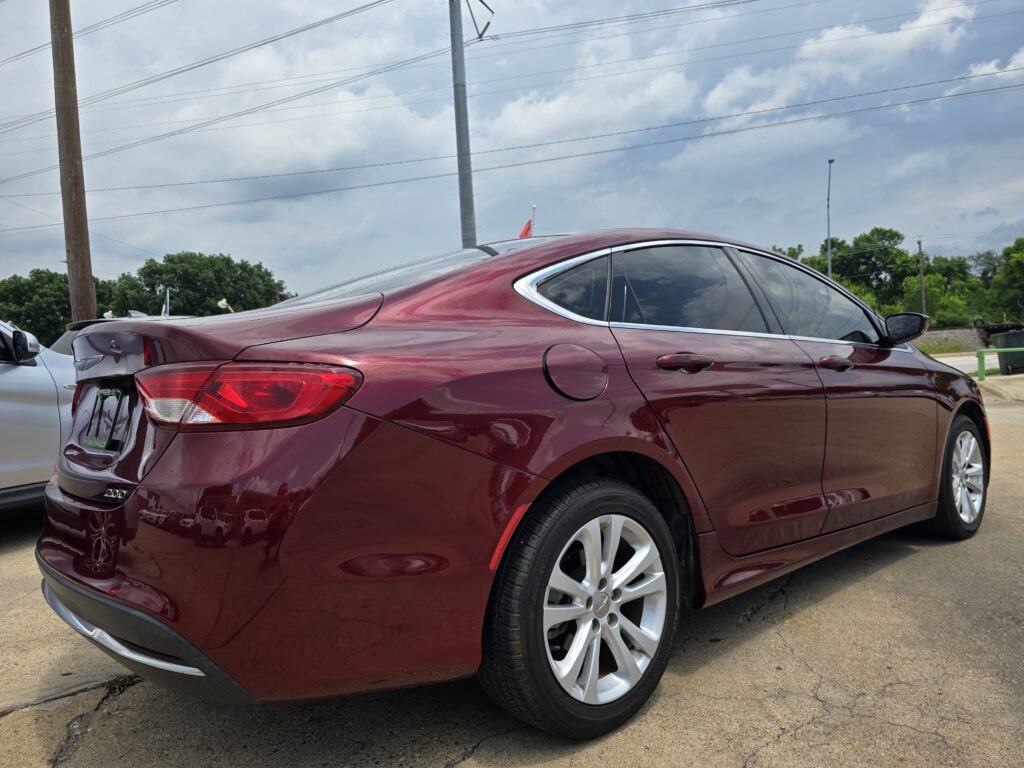 Maroon sedan viewed from the rear side in a parking lot, chrome trim and tinted rear window visible.
