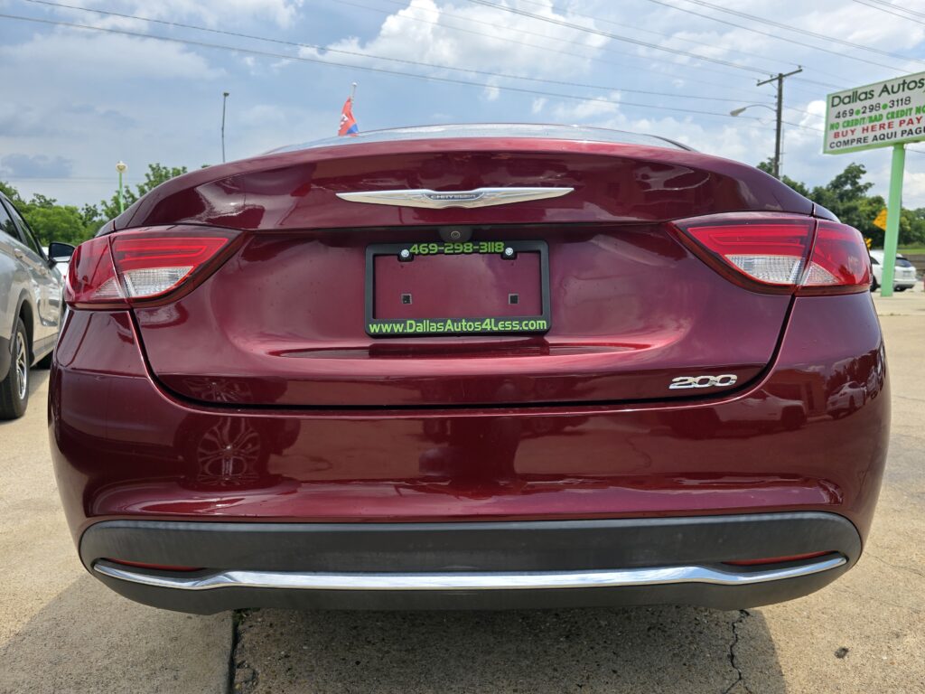 Maroon Chrysler 200 rear view with dealer plate frame, at a lot with a Dallas Autos sign in the background.