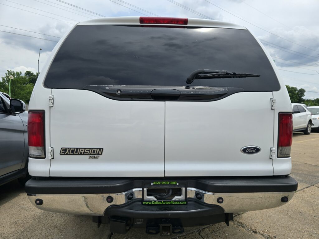Rear view of a white Ford Excursion SUV, showing an scratched/scuffed trim along the tailgate and a dark tinted rear window with wiper present.