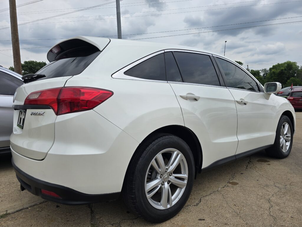 Rear three-quarter view of a white SUV with dark tinted windows and a rear spoiler, parked on a lot.