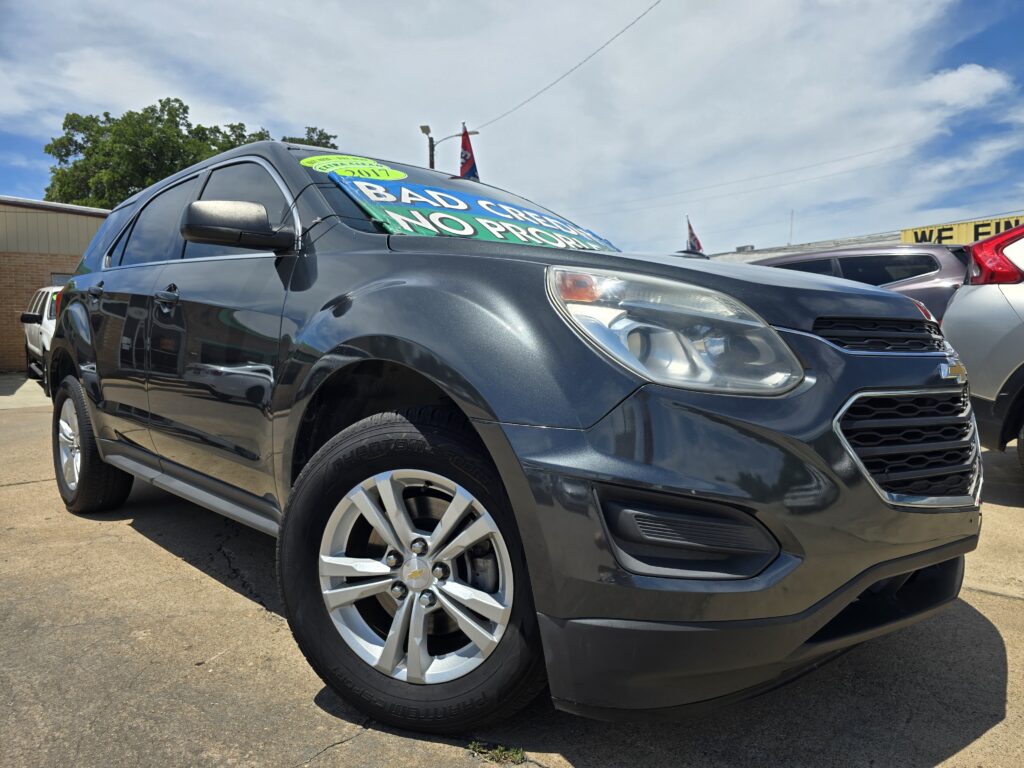 Dark gray SUV at a car dealership with a bright windshield sign reading 'BAD CREDIT NO PROBLEM' under a blue sky