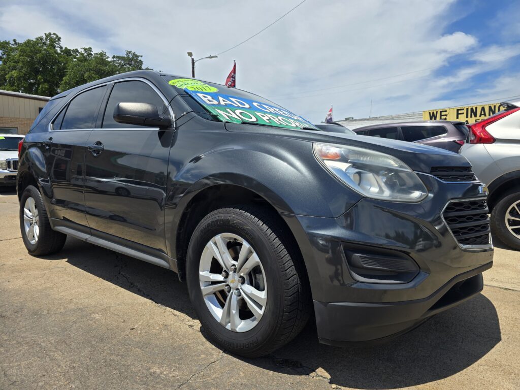 Black SUV with large green sale sign on the windshield at a used-car lot, front-right view.