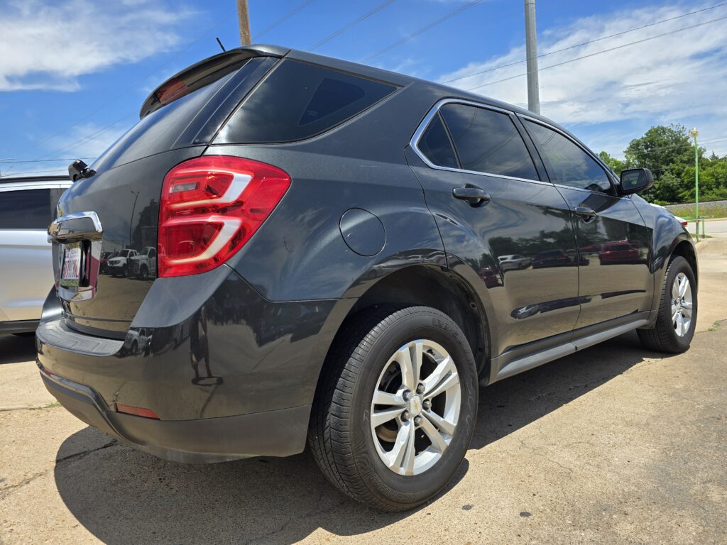 Dark gray SUV viewed from rear-side angle in a parking lot, showing a red taillight, chrome trim, and rear wheel.