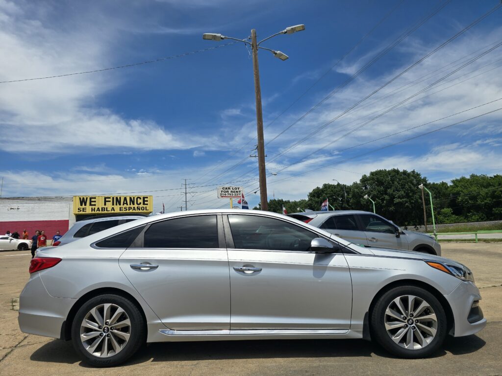 Silver sedan in a parking lot with a bright yellow 'We Finance' sign and power lines against a blue sky.