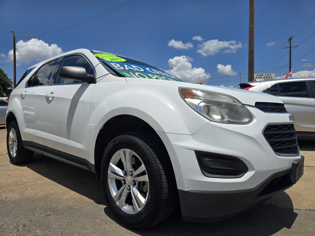 White SUV parked in a car dealership lot with large sale signs on the windshield against a blue sky.