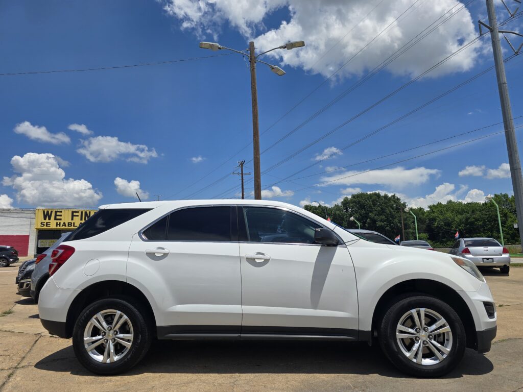 White SUV in a dealership lot with a blue sky,Utility poles, and power lines overhead.
