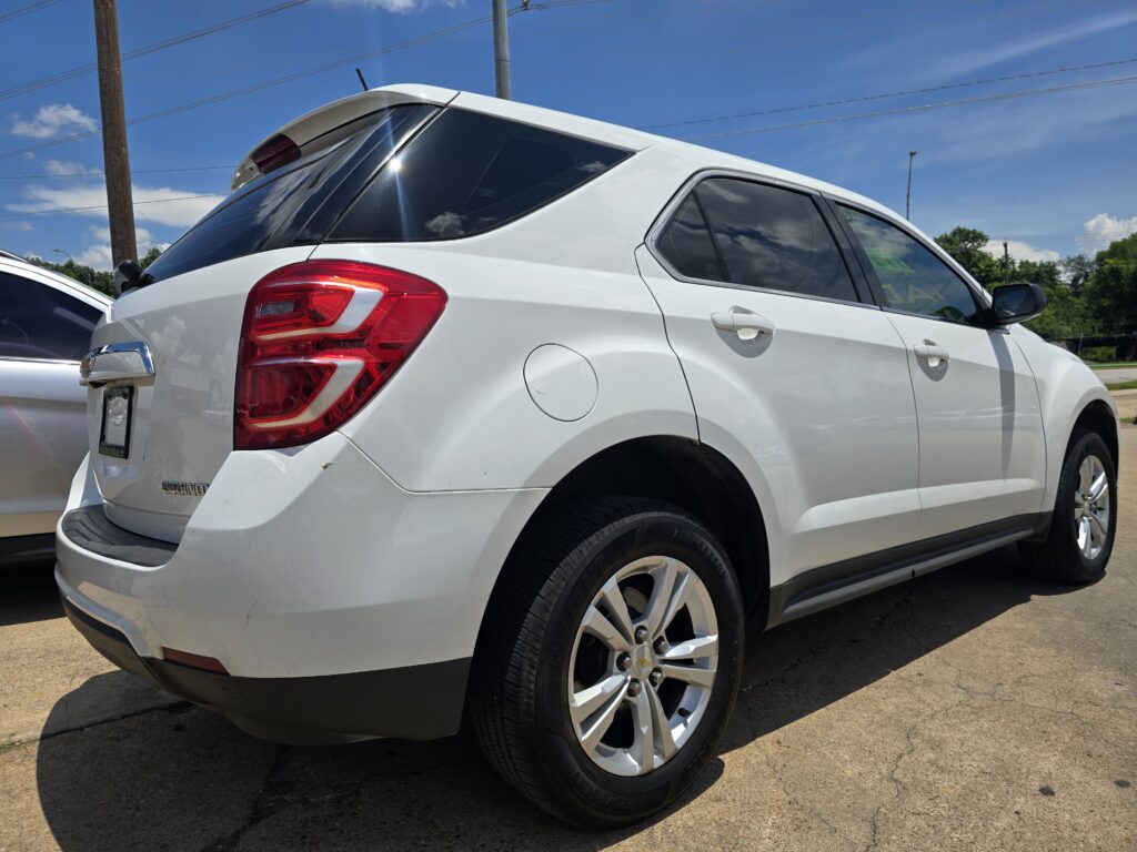 Rear three-quarter view of a white Chevrolet Equinox SUV parked in a sunny lot, showing the taillight, rear hatch, and alloy wheels against a blue sky.