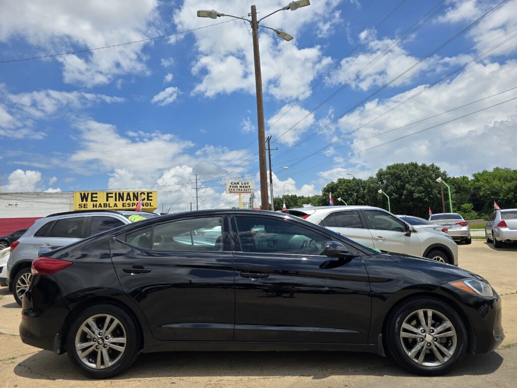 Parking lot full of cars with a bright blue sky and scattered clouds; a yellow 'WE FINANCE' sign is visible in the background.
