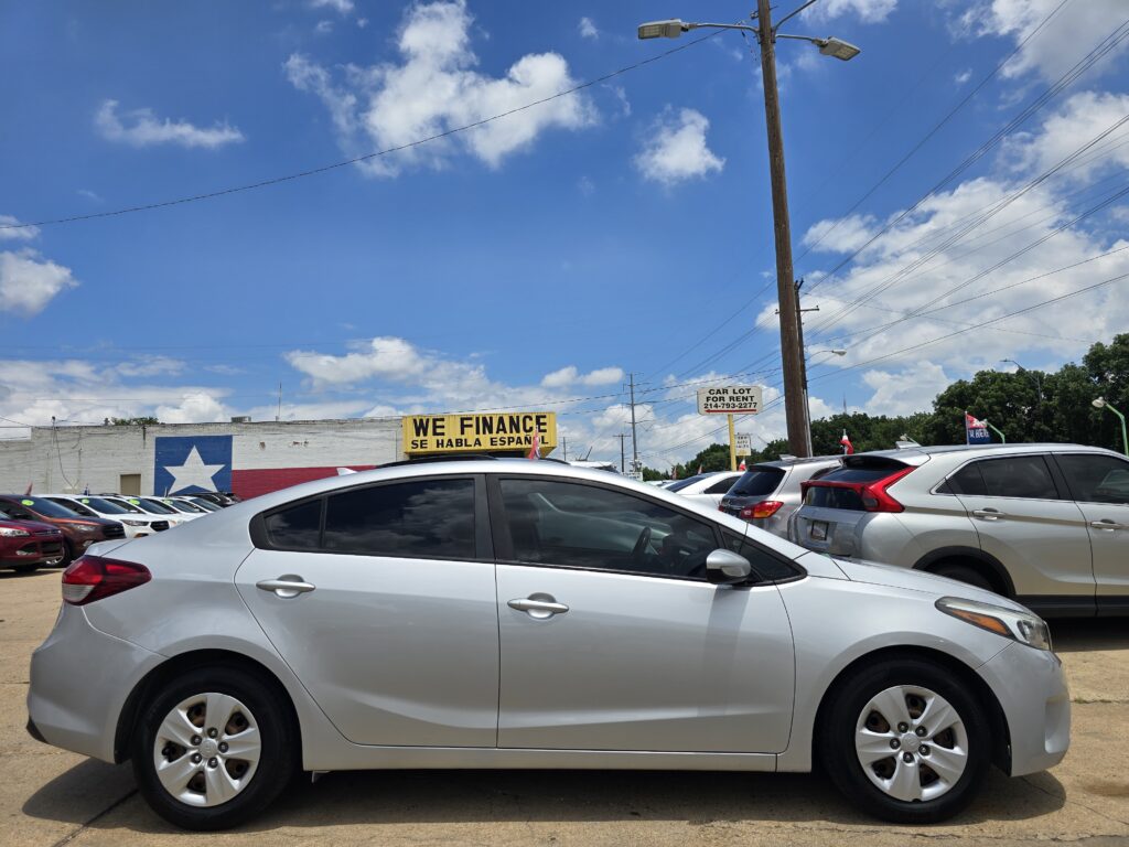 Car dealership lot filled with many parked cars and a bold 'WE FINANCE' banner against a blue sky. Look of a busy used-car lot.