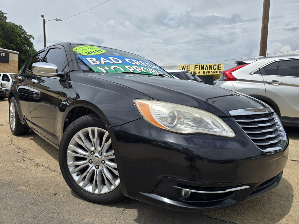 Close-up of a black car on a used-car lot with bold windshield signs and a 'WE FINANCE' banner in the background.
