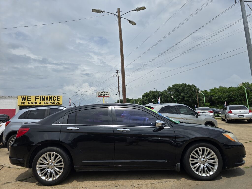 Black SUV in the foreground at a car lot with a yellow 'We Finance' sign and overhead power lines during a cloudy day.
