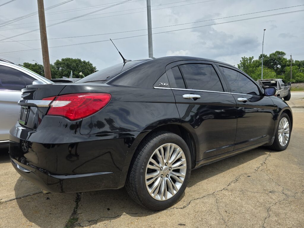 Rear-side view of a black sedan with chrome trim and large alloy wheels parked on a street, showing a '200' badge on the rear window area
