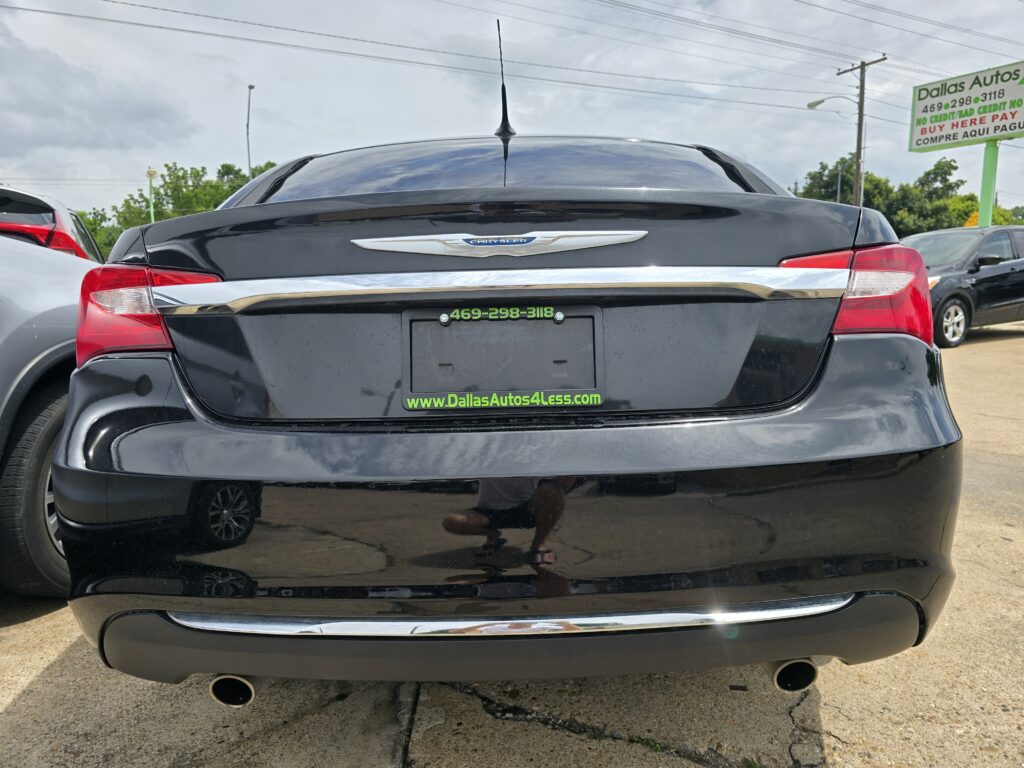 Black Chrysler sedan rear view with shiny chrome trim and red taillights, dealership plate frame reading www.DallasAutos4Less.com on a sunny day.