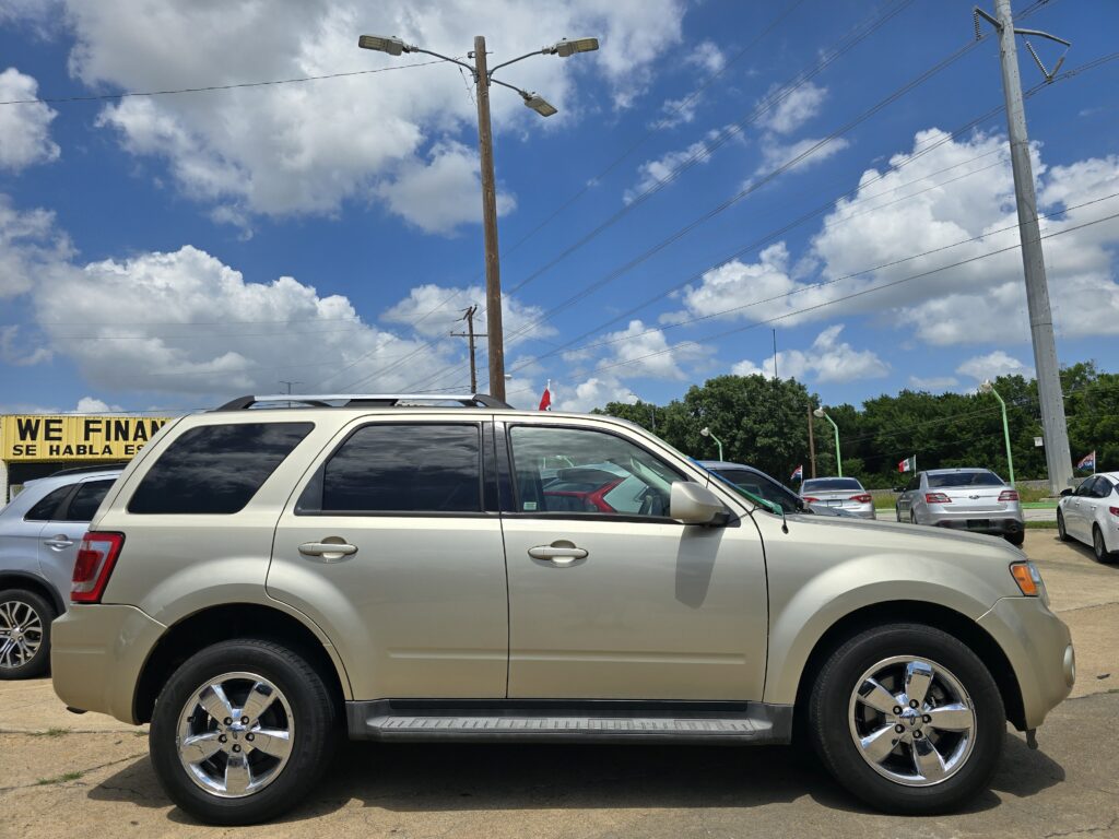 Beige SUV in a car lot on a sunny day, with other vehicles and utility poles against a blue sky.