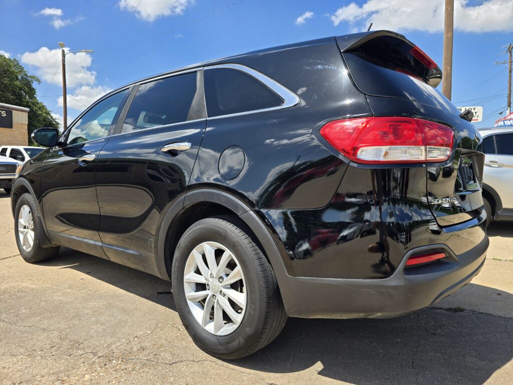 Close-up of a black SUV rear quarter with red taillight, chrome trim, and rear spoiler in a parking lot under a blue sky.
