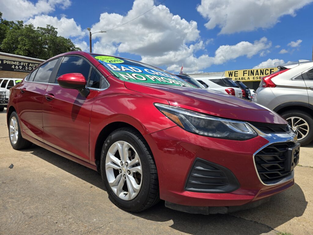 Red sedan in a dealership lot with sale signs on the windshield and a 'We Finance' banner in the background.