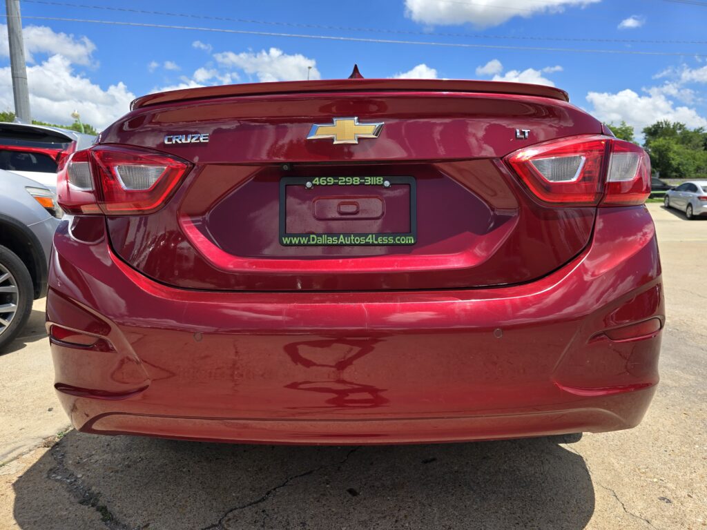 Rear view of a red Chevrolet Cruze LT with chrome bowtie emblem, license plate frame from Dallas Autos 4 Less, in a parking lot.