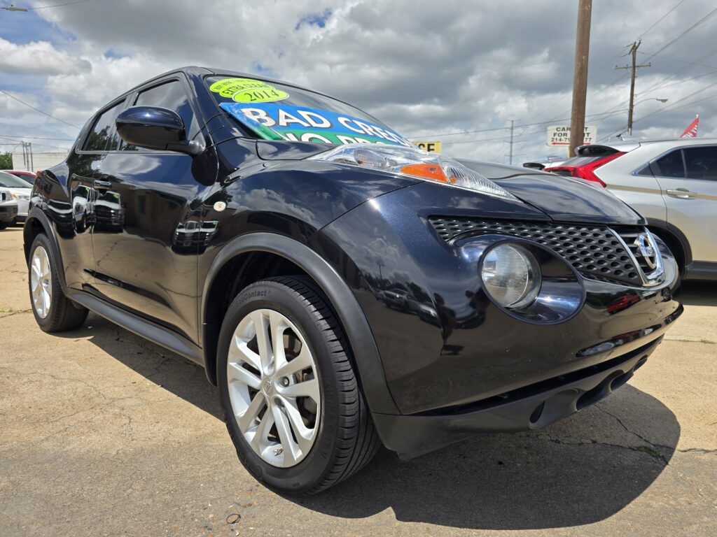 Close-up of a shiny black SUV at a car dealership with large colorful sale signs on the windshield and other cars in the background.